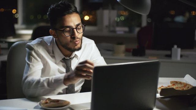 Medium shot of Arab businessman in formalwear and glasses working after hours in dark office