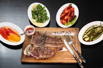 Medium-roasted steak cut into pieces on a wooden board with sauce and seasonings. Delicious steak. Beef steak medium rare on vegetable cushion. Beef steak on wooden plate. 