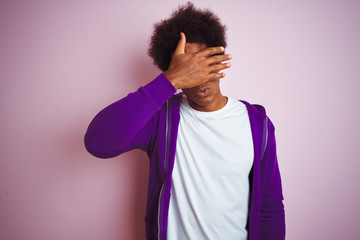 Young african american man wearing purple sweatshirt standing over isolated pink background covering eyes with hand, looking serious and sad. Sightless, hiding and rejection concept