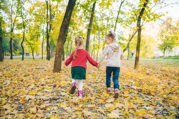 two little girls girlfriends playing at autumn city park holding hands