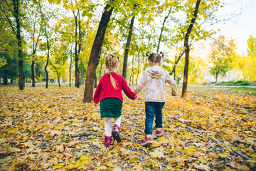 Obraz premium two little girls girlfriends playing at autumn city park holding hands