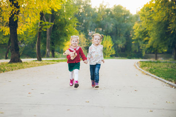 two little girls girlfriends playing at autumn city park holding hands