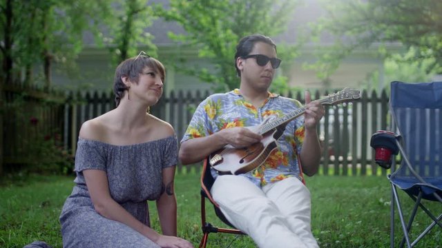 A young hipster couple hang out in the backyard in the summer, the male plays the madeline