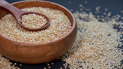 White quinoa seeds on a black background. quinoa in bowl and a spoon on kitchen table top view. Healthy and diet superfood product.