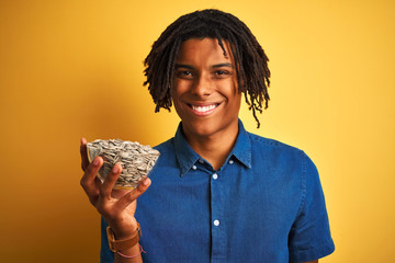 Afro american man with dreadlocks holding sunflowers seeds over isolated yellow background with a...