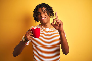 Afro american man with dreadlocks drinking a cup of coffee over isolated yellow background surprised with an idea or question pointing finger with happy face, number one