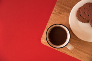 Obraz na płótnie Canvas A white Cup of coffee stands on a wooden Board. Chocolate cookies are on the plate. red background. copy space, flat lay. the view from the top.