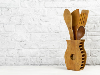 Set of kitchen wooden tools for cooking on non-stick coating. Wooden spoons in a wooden container on kitchen table against the wall. Concept of cooking. Copy space.