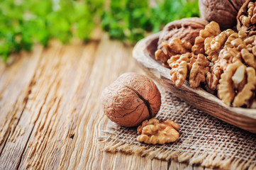 Whole walnuts in wooden bowl. Walnuts concept with green leaves on jute fabric.