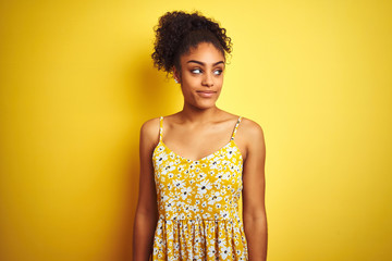 African american woman wearing casual floral dress standing over isolated yellow background smiling looking to the side and staring away thinking.