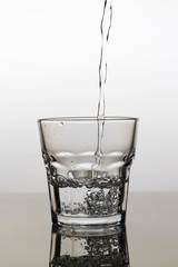 Water is poured into a glass on a light background, close-up