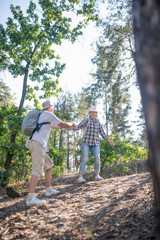 Husband helping wife. Supporting husband wearing backpack helping wife hiking in forest