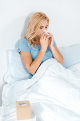 sick woman sneezing in tissue while lying in bed