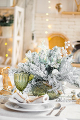 Beautiful served table with decorations, candles with glaze on white tablecloth on the background of the kitchen with people. Living room decorated with lights and Christmas tree.