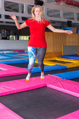 Fitness, fun, leisure and sport activity concept - Young happy woman jumping on a trampoline indoors