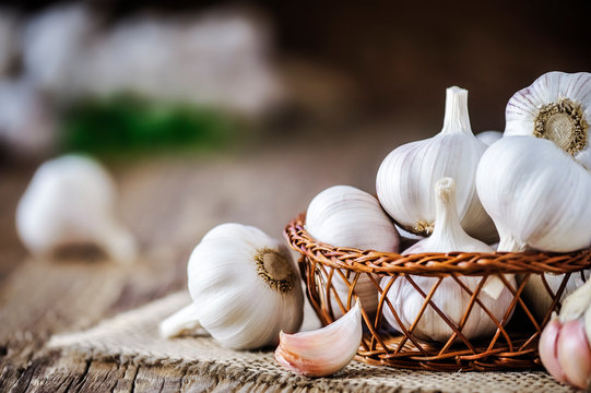 Garlic bulbs in wooden basket on rustic old table. Fresh gralic cloves. Pile of garlic on jute.