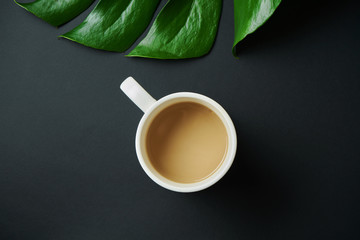 Great Stylish Mock up with coffee in a white cup on a black background with a green tropical leaf. Top view. Flat lay. Morning concept