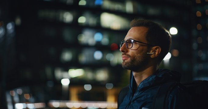 Portrait of an young business man is wearing handsfree earphones in the evening in a city center.