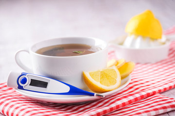 Thermometer with hot tea for illness prevention. Woman is squezzing and pouring lemon juice into tea in sick days. Digital thermometer with fresh tea and lemon concept.
