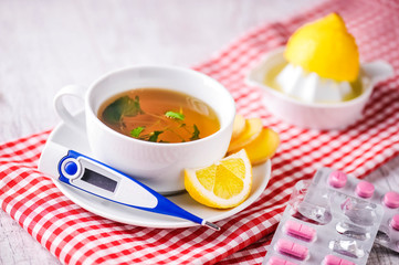 Thermometer with hot tea for illness prevention. Woman is squezzing and pouring lemon juice into tea in sick days. Digital thermometer with fresh tea and lemon concept.