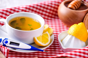 Thermometer and cup of tea with lemon on wooden tray. Honey in background with honey stick.