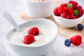 Fresh white yoghurt with raw forest fruits. Rasberries in white yoghurt in bowl on white table. Best meal for healthy breakfast.