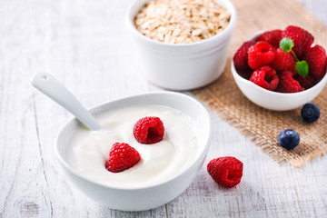 Fresh white yoghurt with raw forest fruits. Rasberries in white yoghurt in bowl on white table. Best meal for healthy breakfast.