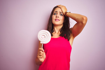 Young beautiful woman eating sweet candy over pink isolated background stressed with hand on head, shocked with shame and surprise face, angry and frustrated. Fear and upset for mistake.