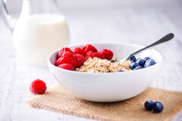 Oat flakeswith forest fruits in white plate on rustic table with jar of milk in backgrund.