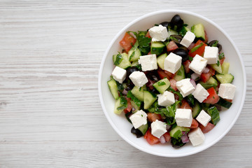 Homemade Shepherd's salad with cucumbers, feta and parsley in a white bowl on a white wooden table,...