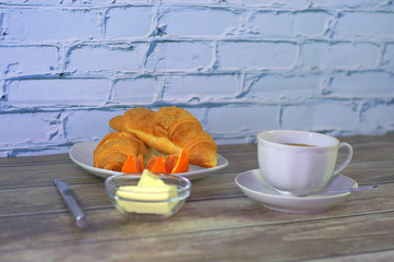 A hearty breakfast, a cup of black coffee, two croissants, slices of orange and butter.