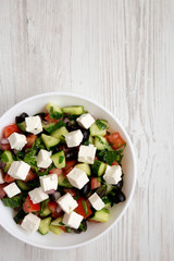 Homemade Shepherd's salad with cucumbers, feta and parsley in a white bowl on a white wooden background, top view. From above, overhead.