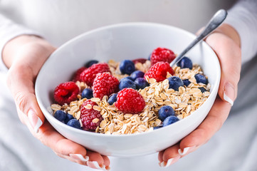 Oat flakes with forest fruits in white plate. Plate full of oat flakes and raspberries, blueberries in woman hands.