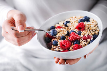 Oat flakes with forest fruits in white plate. Plate full of oat flakes and raspberries, blueberries in woman hands.