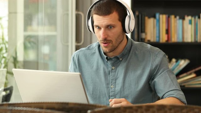 Excited man wearing headphones reading content on laptop finding offers sitting in a coffee 