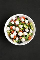Homemade Shepherd's salad with cucumbers, feta and parsley in a white bowl over black surface, top...