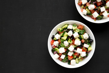 Homemade Shepherd's salad with cucumbers, feta and parsley in white bowls on a black background, top view. From above, overhead, flat lay. Copy space.