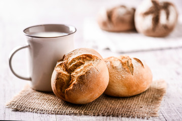 Fresh buns and jar of milk on jute. Dark and light rolls of tasty and  beautiful bread on rustic white table.