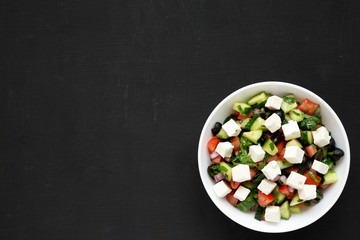 Homemade Shepherd's salad with cucumbers, feta and parsley in a white bowl over black surface, top view. From above, overhead, flat lay. Copy space.