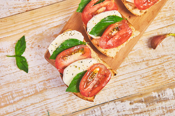Caprese bruschetta toasts on a cutting board. Bruschetta with tomatoes, mozzarella cheese and basil on a rustic table. Traditional italian appetizer or snack, antipasto
