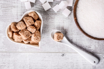 White fresh sugar on white table. Sugar in wood bowl. Brown sugar in heart bowl with spoon and brown cube.