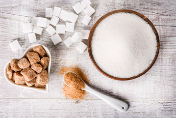 Obraz na płótnie Canvas White fresh sugar on white table. Sugar in wood bowl. Brown sugar in heart bowl with spoon and brown cube.