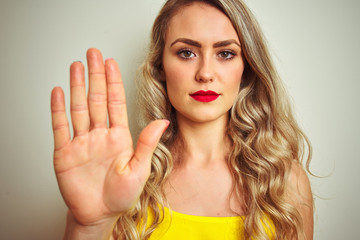 Young beautiful woman wearing yellow t-shirt standing over white isolated background with open hand doing stop sign with serious and confident expression, defense gesture