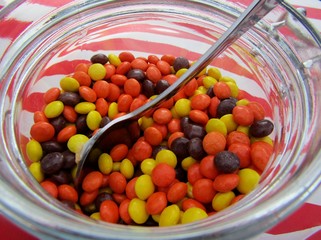 Red, yellow and brown peanut butter pieces with spoon in container for DIY cupcake station