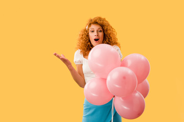 surprised redhead girl with pink balloons isolated on yellow