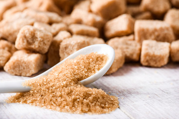Brown sugar cubes on white rustic table. Brown sugar in white spoon.