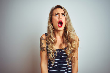 Young beautiful woman wearing stripes t-shirt standing over white isolated background angry and mad screaming frustrated and furious, shouting with anger. Rage and aggressive concept.