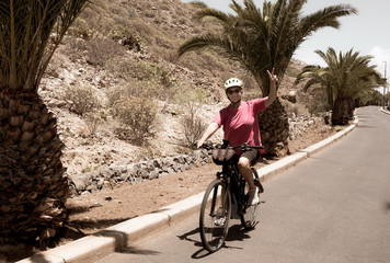 An elderly woman enjoying bicycle with a modern e bike. Background of mountain and palm trees. One people.Healthy activity for retired person.