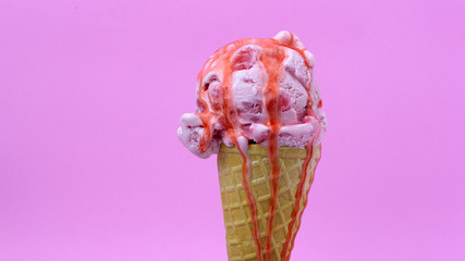 Strawberry ice cream scoop in waffle cone with  Strawberry sauce on pink background, Closeup Front view Food concept..