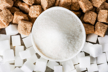 Sugar on white table in bowl. Sugar cubes brown and white from top view.